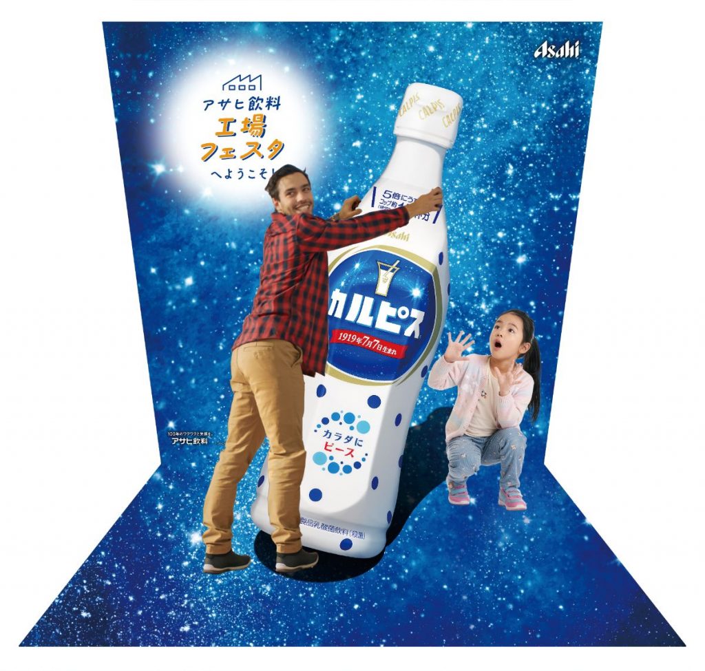 アサヒ飲料カルピスの巨大ボトルを支えるポーズで撮れるオリジナルトリックアート。工場イベントのフォトスポット